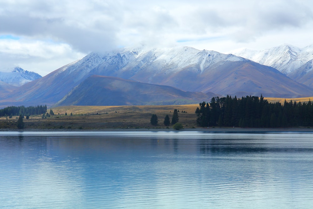 lake near green trees and mountain under white clouds and blue sky during daytime