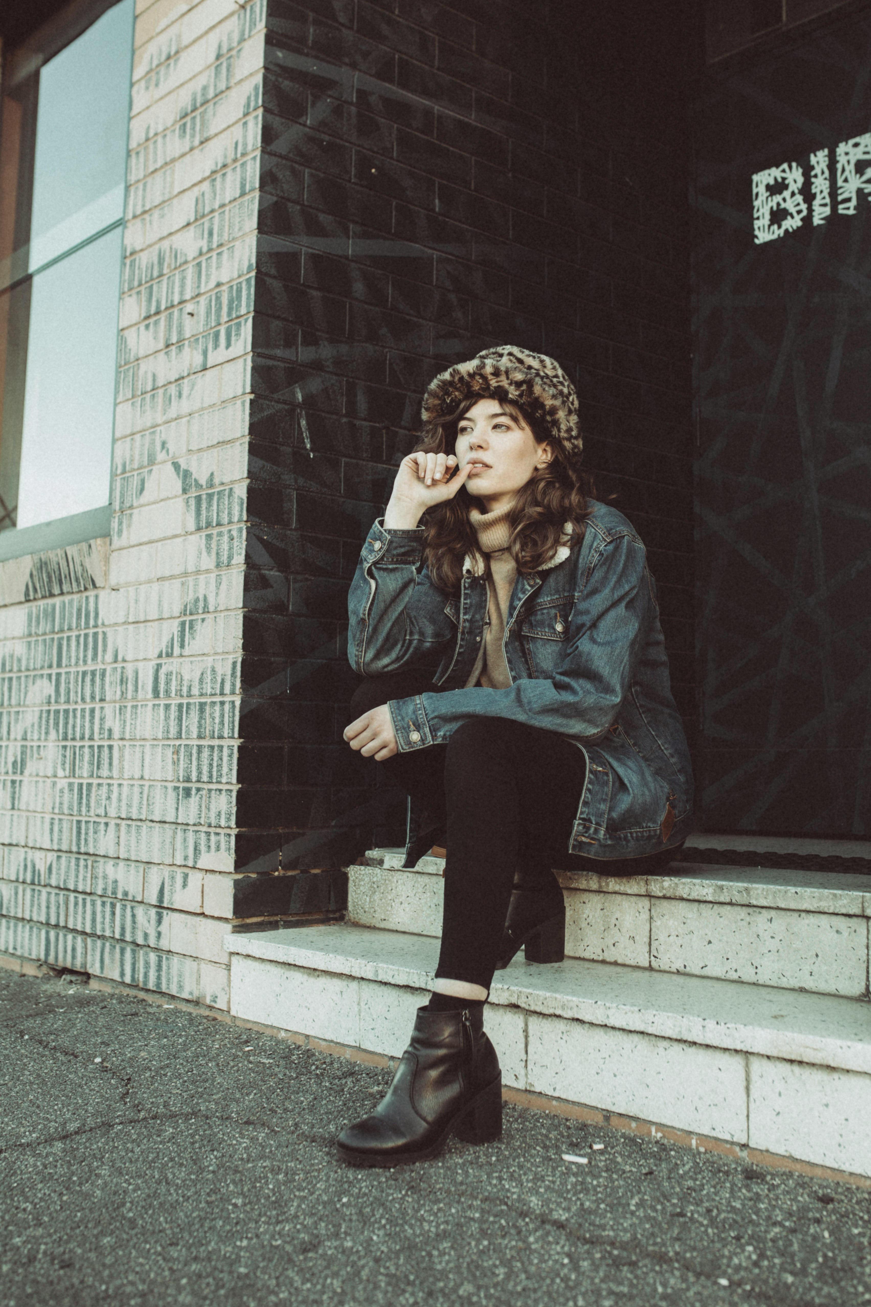 woman in blue denim jacket and black pants sitting on gray concrete stairs