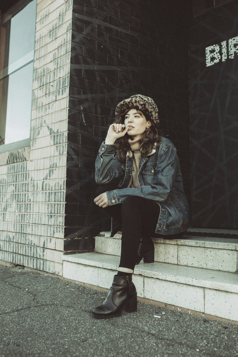 woman in blue denim jacket and black pants sitting on gray concrete stairs