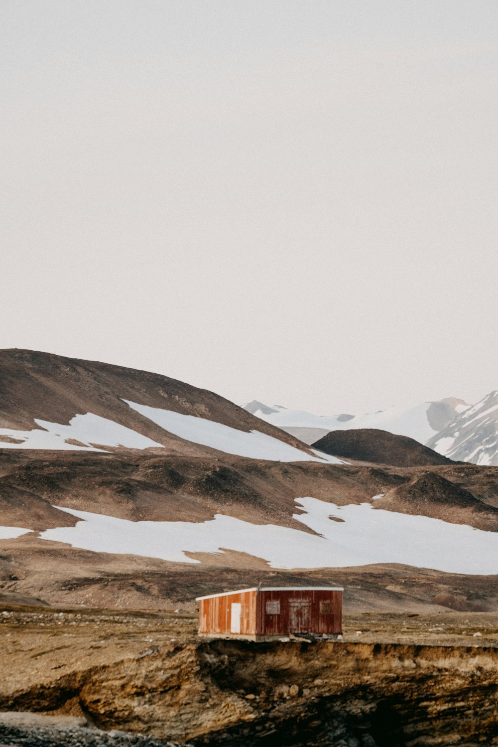 brown wooden house on brown field near snow covered mountain during daytime