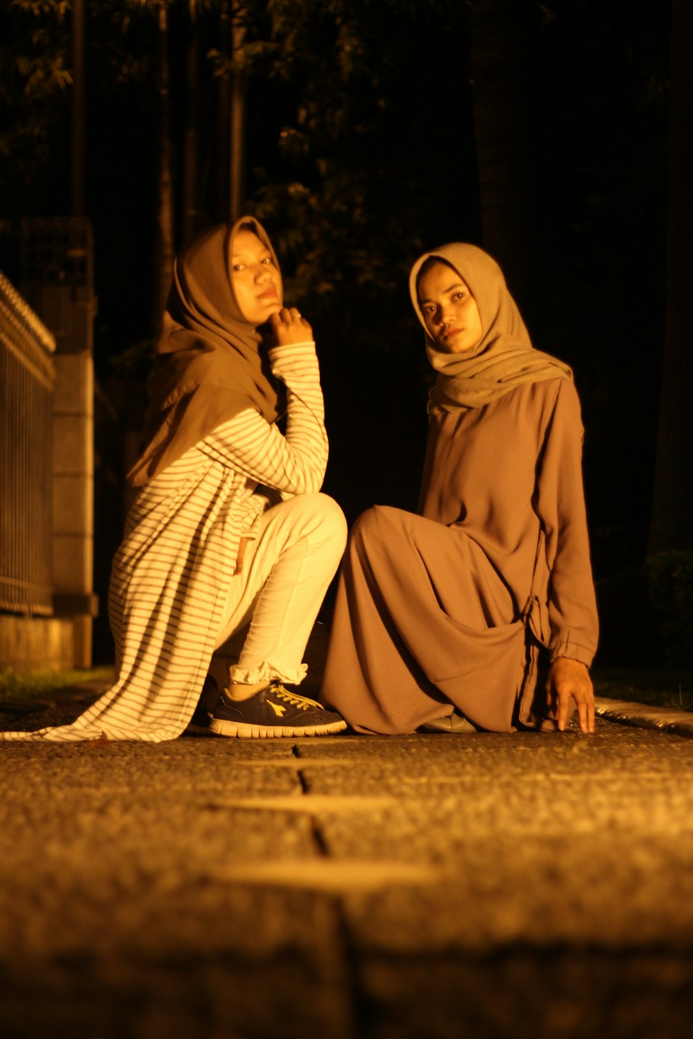 2 women in brown hijab sitting on brown concrete floor