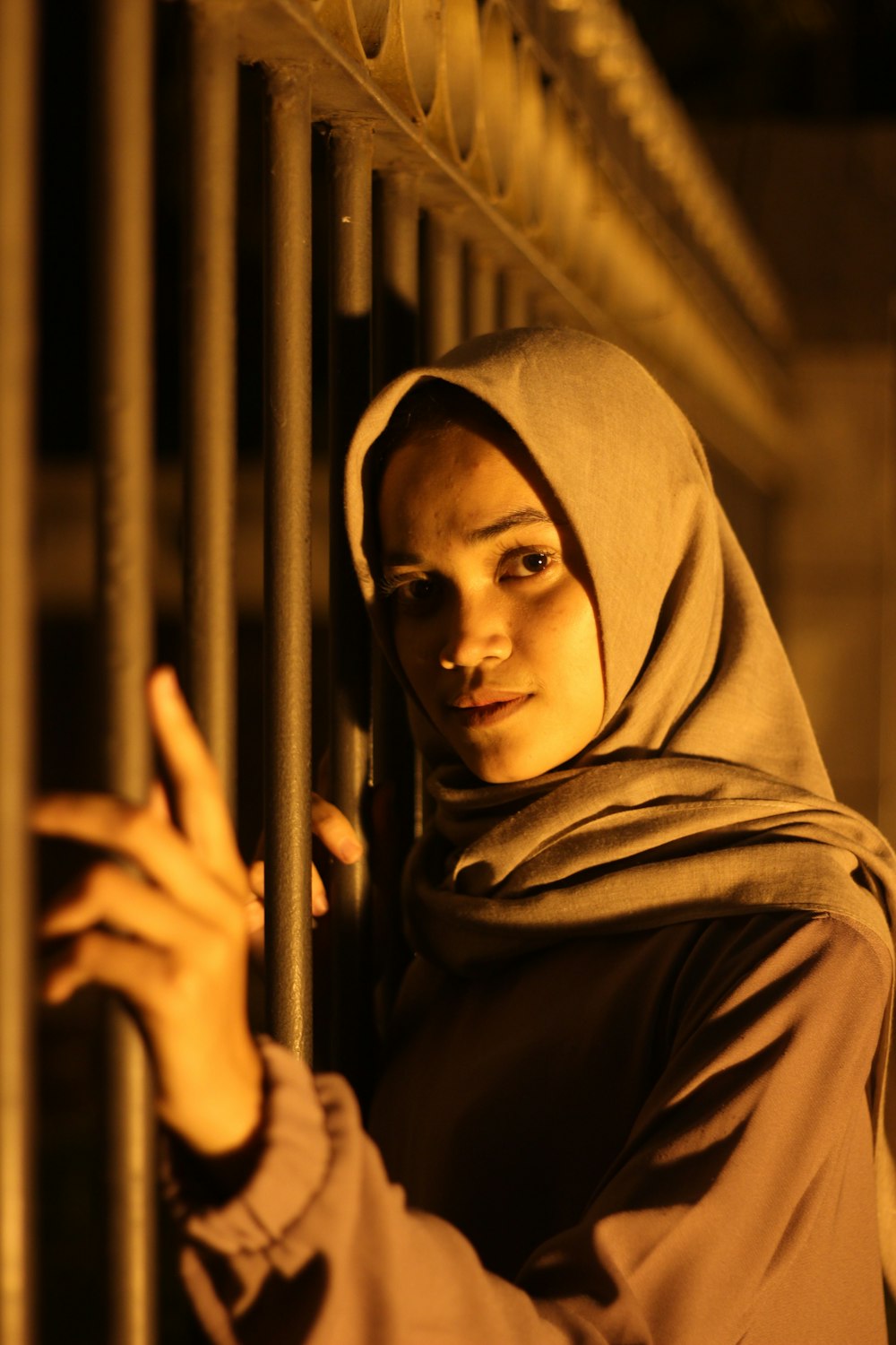 woman in brown hijab standing near brown metal fence