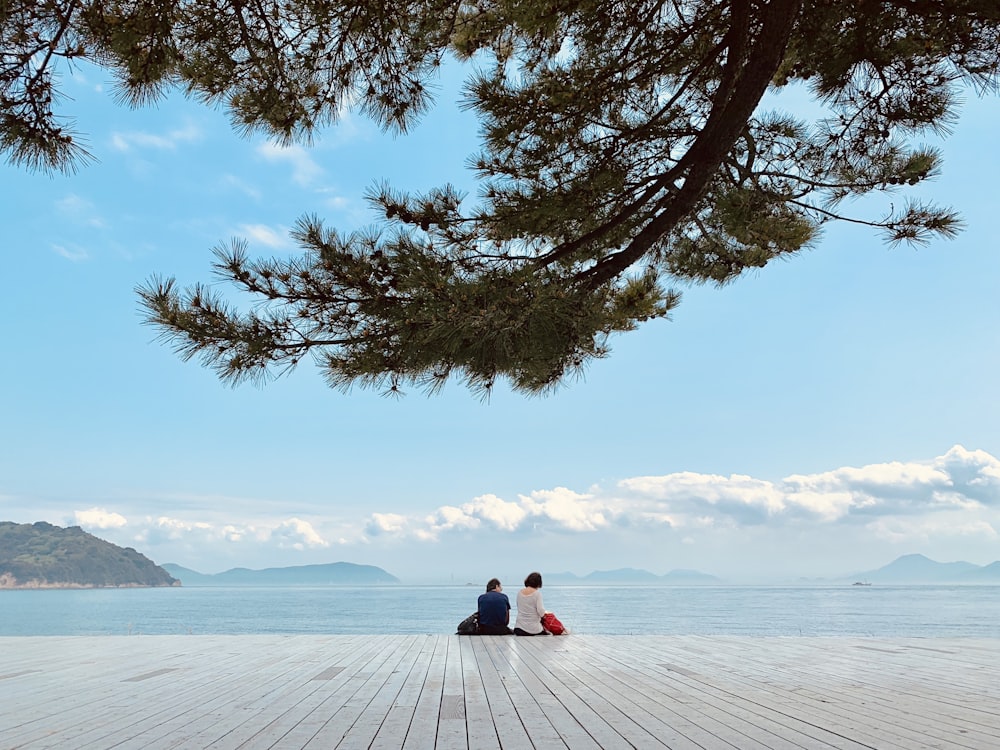 person sitting on white snow covered ground near body of water during daytime