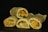 Four rolled wraps filled with a colorful assortment of vegetables, including carrots, greens, and what appears to be zucchini, resting against a dark background. The wraps have a slightly speckled texture.