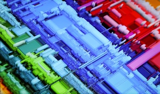 A vibrant, abstract 3D geometric structure composed of colorful blocks and layered forms. The intricate design consists of rectangles and squares in various sizes, creating a sense of depth and complexity. The colors transition smoothly from cool blues and greens on the left to warm reds on the right.