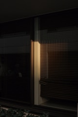 Dark and moody interior window with closed blinds casting shadows. A beam of warm light softly illuminates one section, adding a subtle contrast to the surrounding darkness.