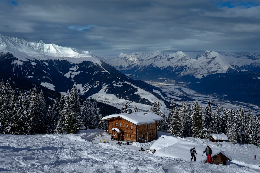 brown wooden house on snow covered ground near snow covered mountain during daytime