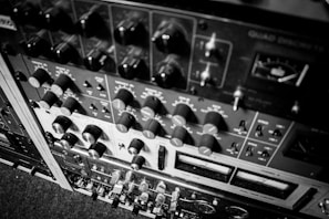 A detailed view of various audio equipment, including knobs, switches, and meters arranged in a rack. The equipment appears to be vintage audio processing units, possibly used for mixing or recording purposes.