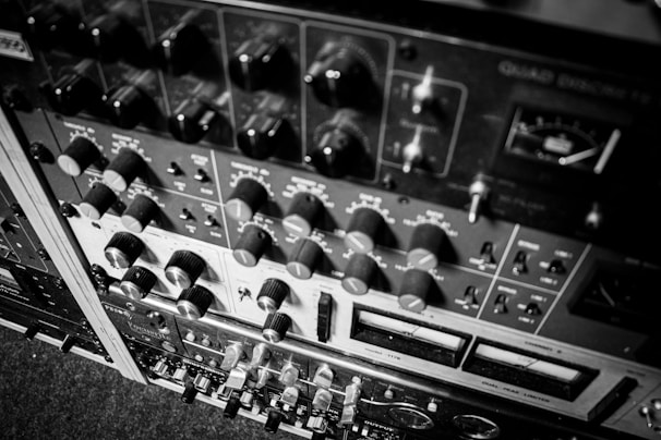 A detailed view of various audio equipment, including knobs, switches, and meters arranged in a rack. The equipment appears to be vintage audio processing units, possibly used for mixing or recording purposes.