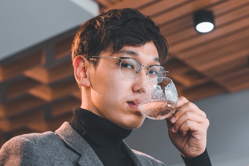 man in black framed eyeglasses holding clear drinking glass
