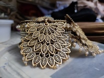 Intricate jewelry design featuring leaf-shaped patterns adorned with small, detailed embellishments. The craftsmanship includes a combination of gold and black materials, giving it an exquisite and luxurious appearance.