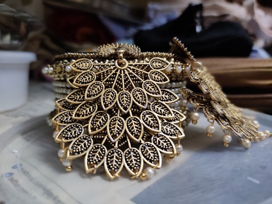Intricate jewelry design featuring leaf-shaped patterns adorned with small, detailed embellishments. The craftsmanship includes a combination of gold and black materials, giving it an exquisite and luxurious appearance.