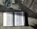An open book with text in a language that appears to be Chinese is placed on a textured surface. There is a glass of water nearby, showing light reflections and refractions. Part of a newspaper with visible text is placed adjacent to the book, adding a sense of casual reading or study.