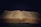 An open book rests against a dark background, the pages filled with small, printed text. The book's cover is textured with a golden hue, and a thin ribbon bookmark lies in the center.