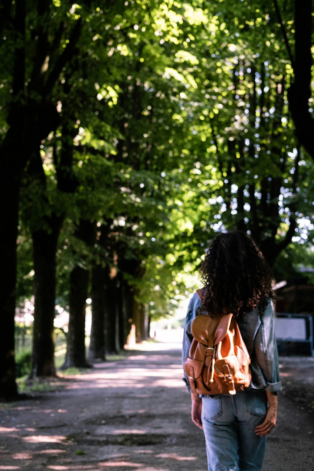 woman in brown and white dress walking on pathway between green trees during daytime