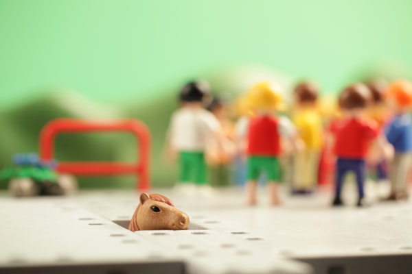 a toy horse coming up through a hole in a game board, with human figures in the background