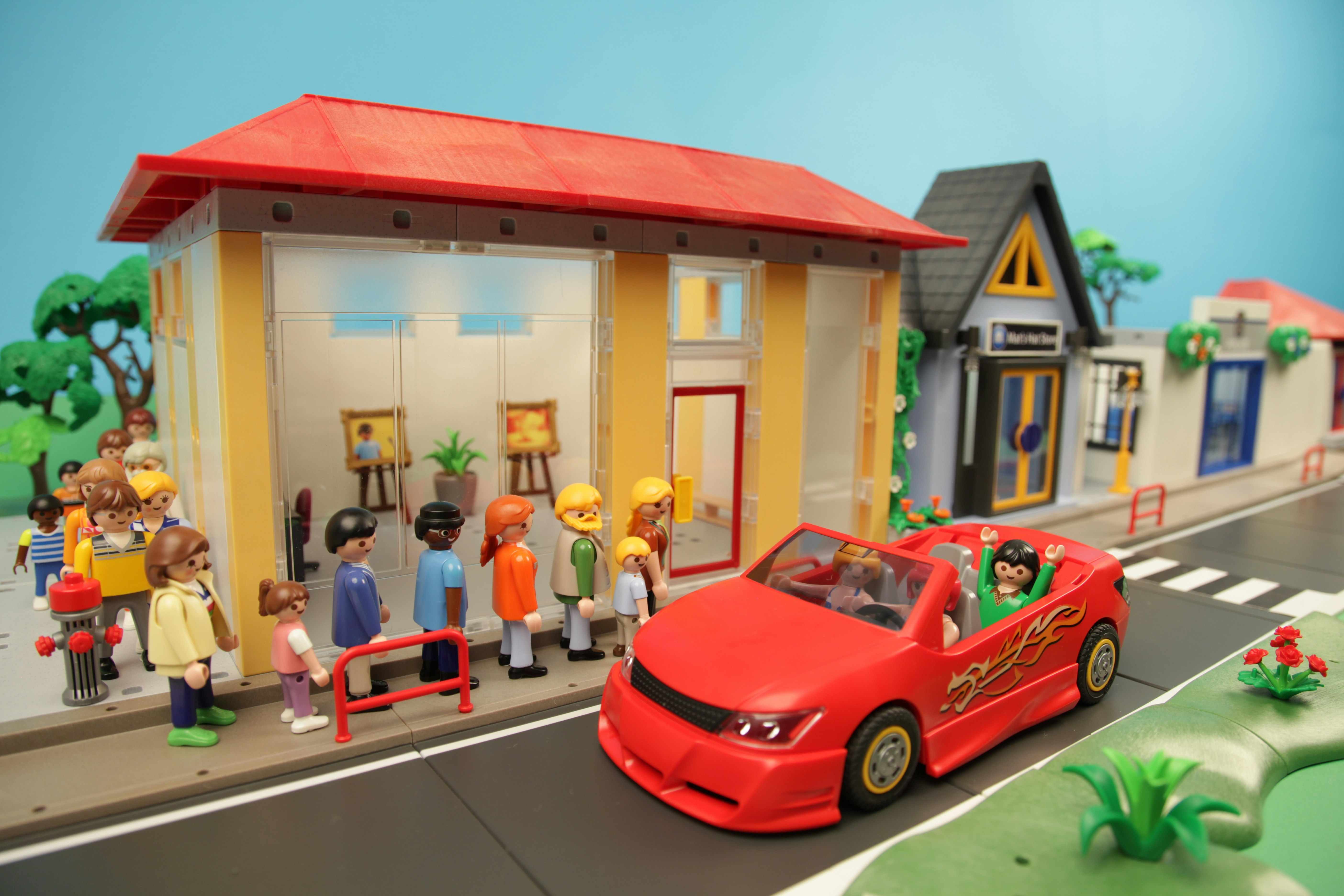 Playmobil people queuing for a gallery while a fancy red sports car whizzes past.