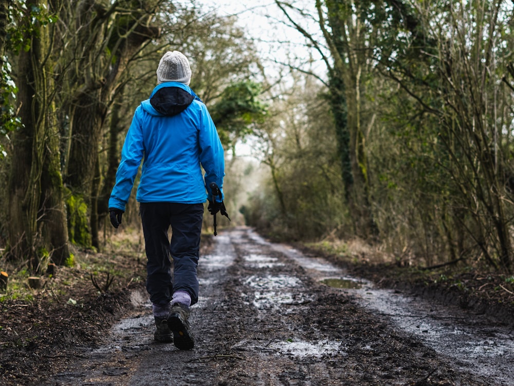 person in blue hoodie walking on dirt road during daytime