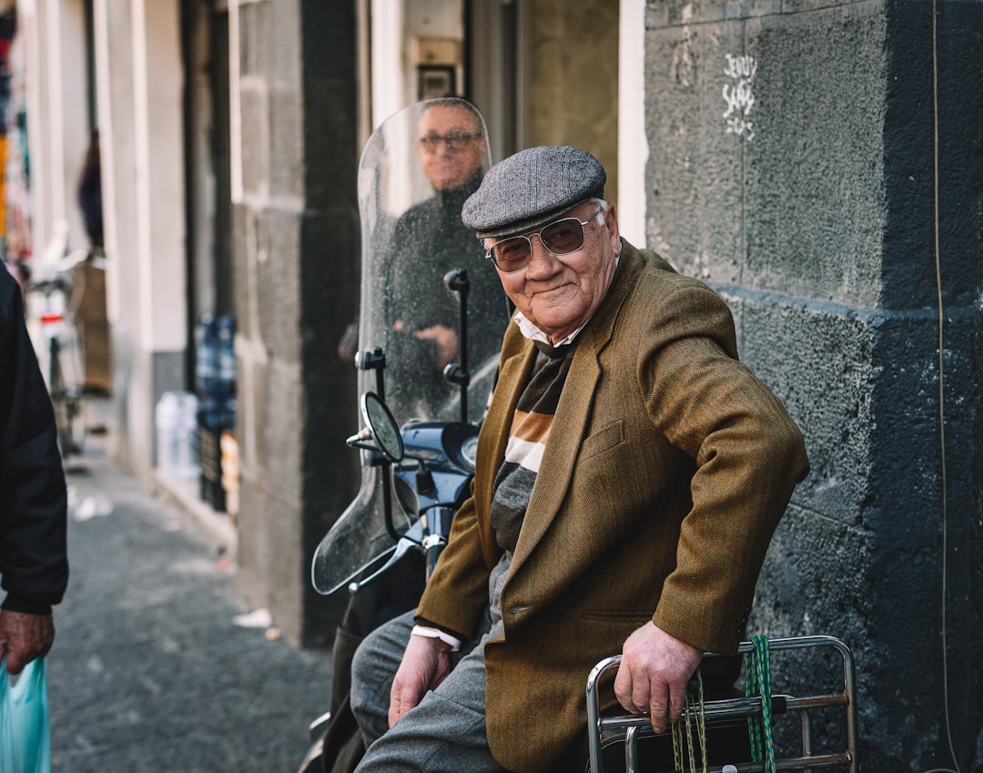 man in brown coat and blue denim jeans sitting on black metal bench during daytime