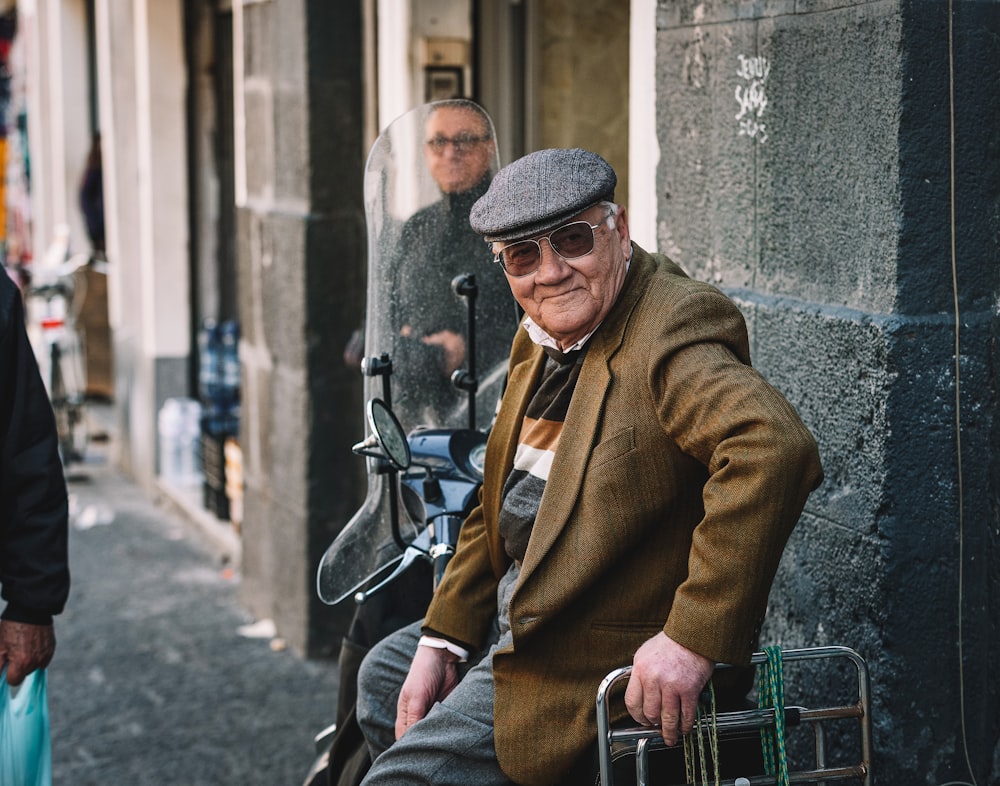 man in brown coat and blue denim jeans sitting on black metal bench during daytime