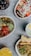 An assortment of colorful food items arranged in bowls on a textured surface. Each dish features fresh ingredients such as fruits, vegetables, and grains with vibrant toppings. Beverages accompany the dishes, enhancing the display with various colors.