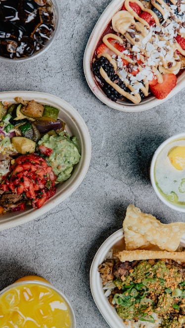 A vibrant spread of colorful bowls, sandwiches, and fresh salads arranged on a rustic wooden table.