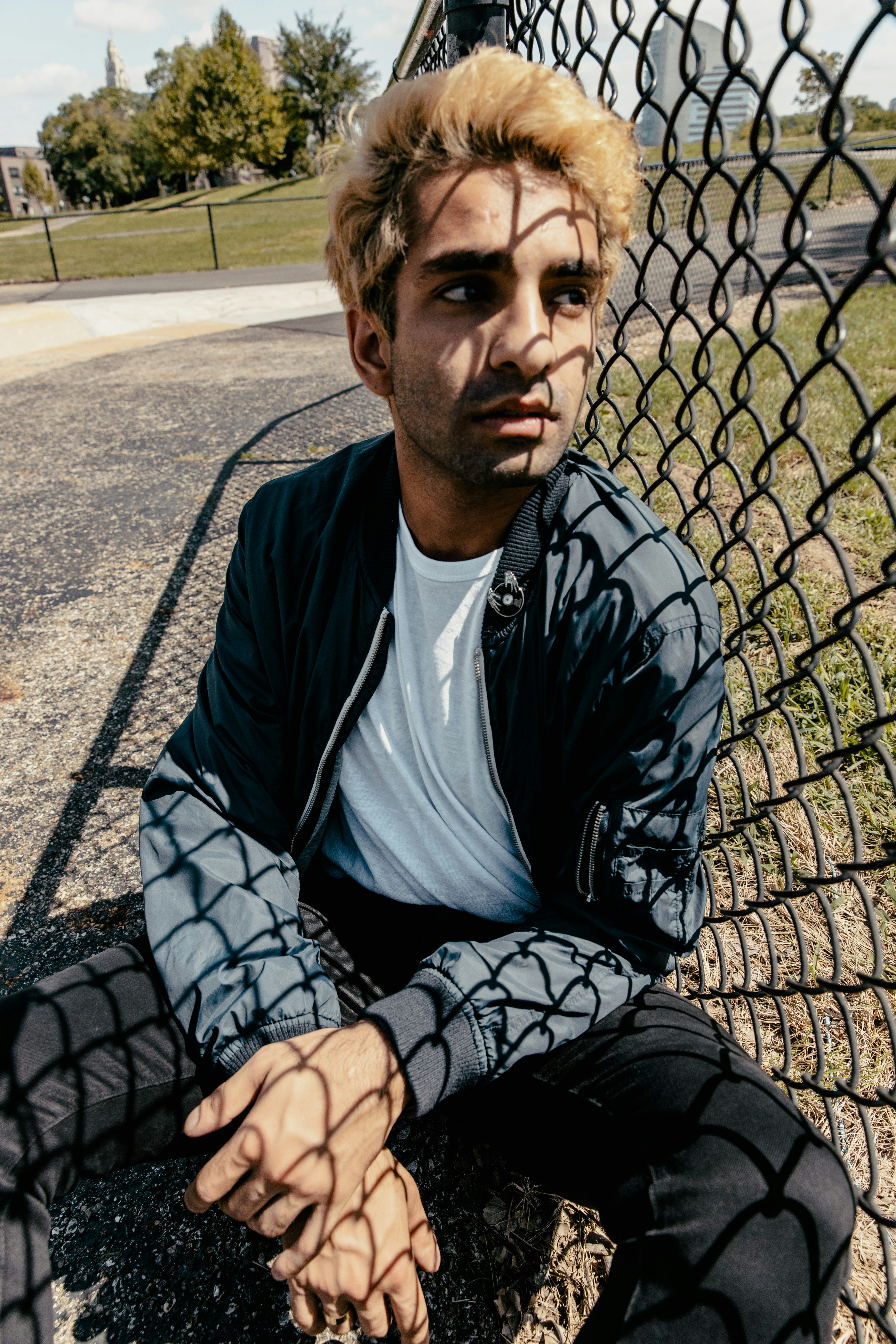 Hombre en chaqueta adidas blanco y negro sentado en piso de concreto gris