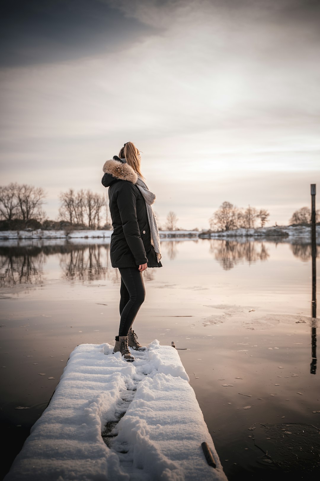 woman in black coat standing on snow covered ground near lake during daytime