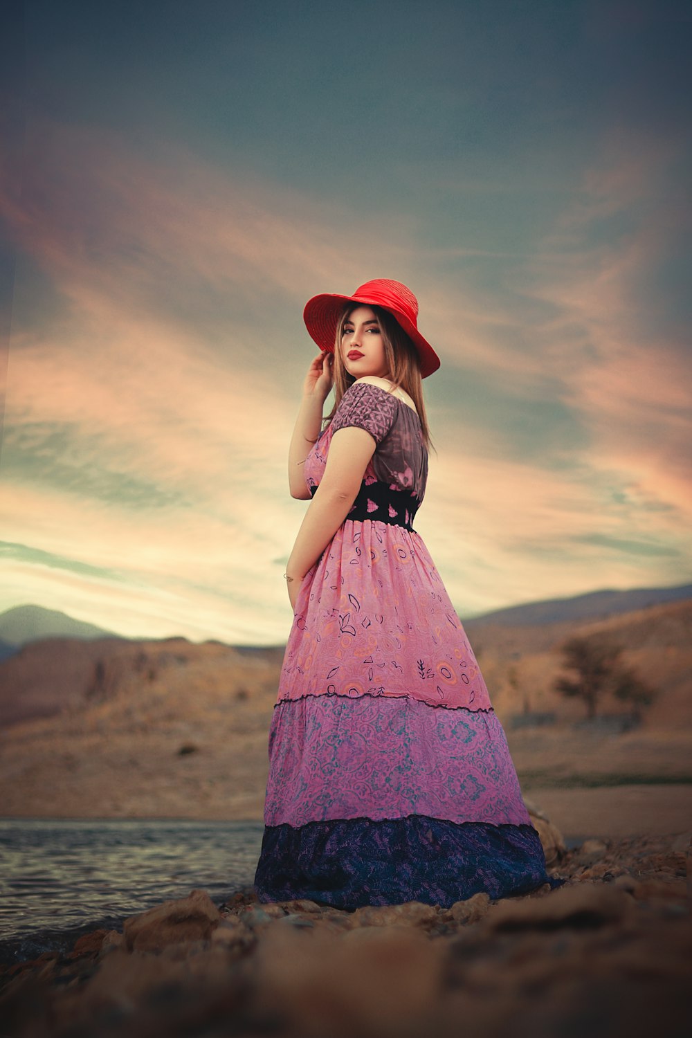 夕暮れ時に茶色の野原に立つ赤い帽子と黒と白のドレスを着た女性
