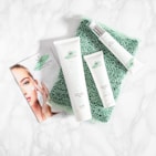 A collection of skincare products labeled with the brand 'Crystalweed', featuring a woman applying cream on her face in a promotional flyer. The products are placed on a textured green surface against a marble background.