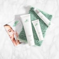A collection of skincare products labeled with the brand 'Crystalweed', featuring a woman applying cream on her face in a promotional flyer. The products are placed on a textured green surface against a marble background.