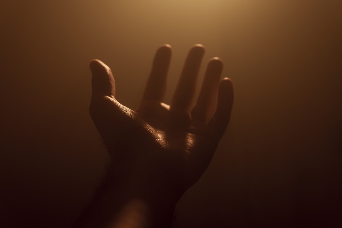 A close-up of a hand reaching out toward a warm light.