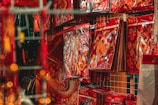 A shelf in a store is filled with vibrant red and gold decorative packets, each featuring cheerful cartoonish images and Chinese characters. The primary figure in these decorations appears to be an ox, often associated with the Chinese zodiac. The packets are neatly stacked against a grid-like background.