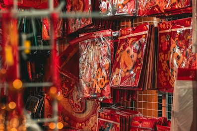 A shelf in a store is filled with vibrant red and gold decorative packets, each featuring cheerful cartoonish images and Chinese characters. The primary figure in these decorations appears to be an ox, often associated with the Chinese zodiac. The packets are neatly stacked against a grid-like background.
