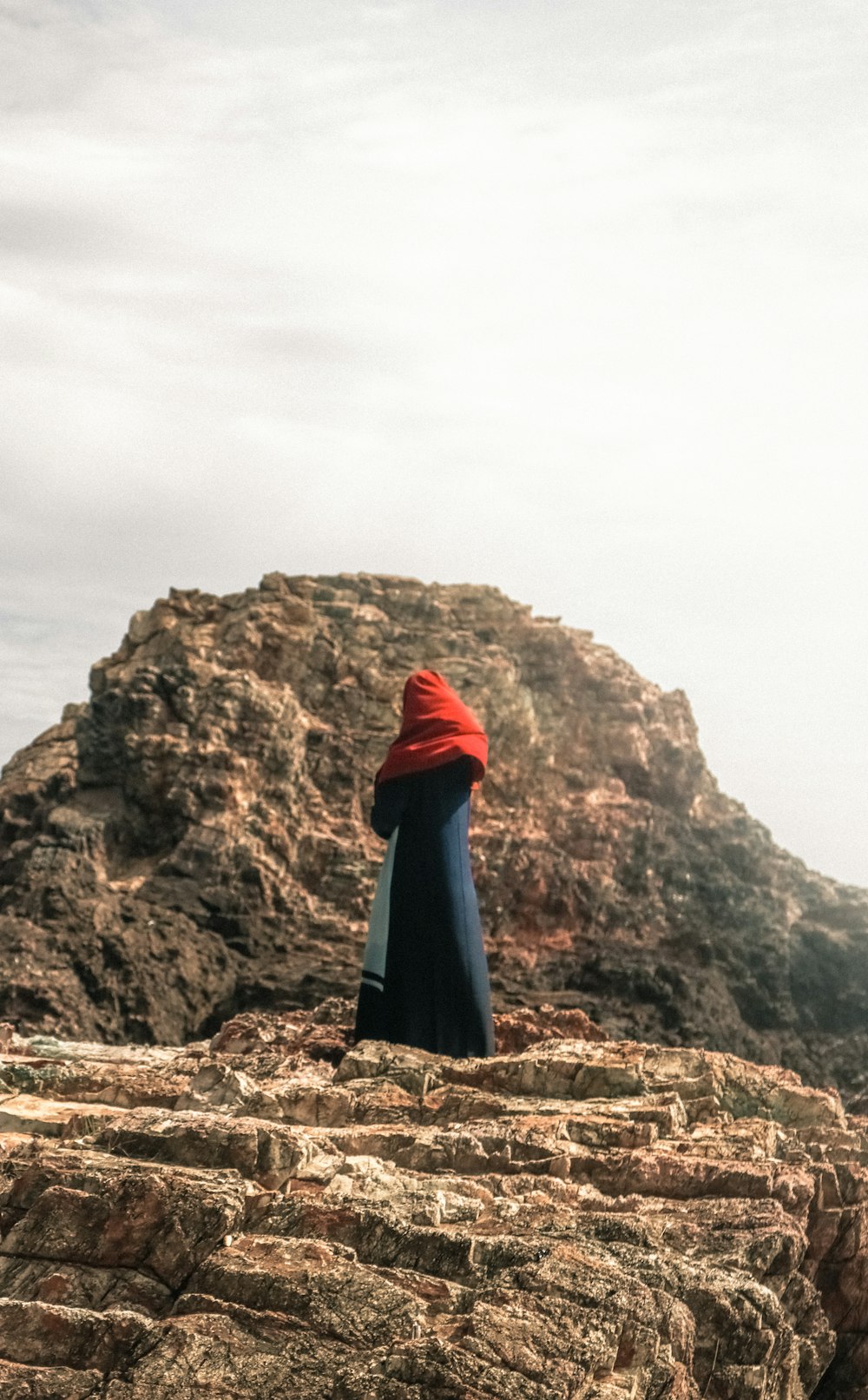 person in red hoodie standing on brown rock formation during daytime