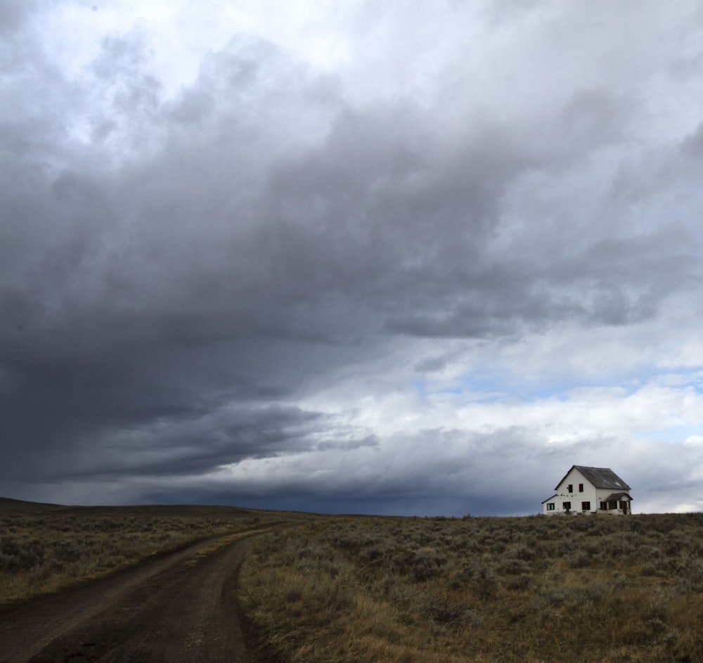 a house in the middle of a field under a cloudy sky