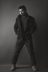 A vertical image of a man in a tailored black jacket standing against a clean white background.