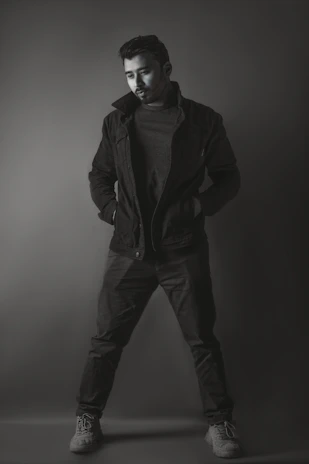 A sleek, minimalist photo of a man wearing a tailored black jacket and crisp white shirt, standing against a soft gray background.