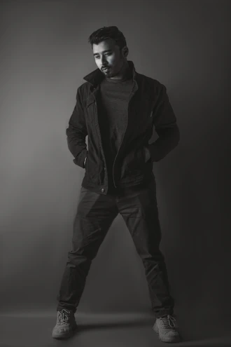 A sleek, minimalist photo of a man wearing a tailored black jacket and crisp white shirt, standing against a soft gray background.