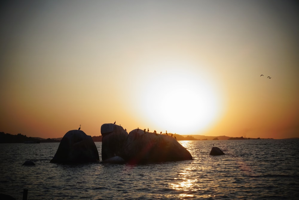 silhouette of rock formation on sea during sunset