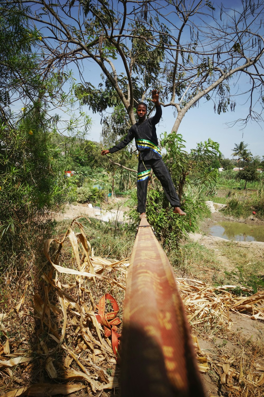 man in black jacket and blue denim jeans jumping on brown wooden log near river during