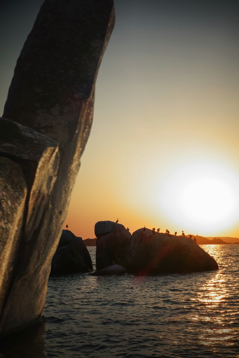 silhouette of rock formation on sea during sunset