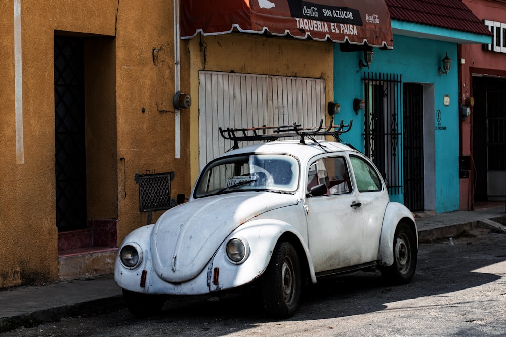 white volkswagen beetle parked beside brown concrete building during daytime