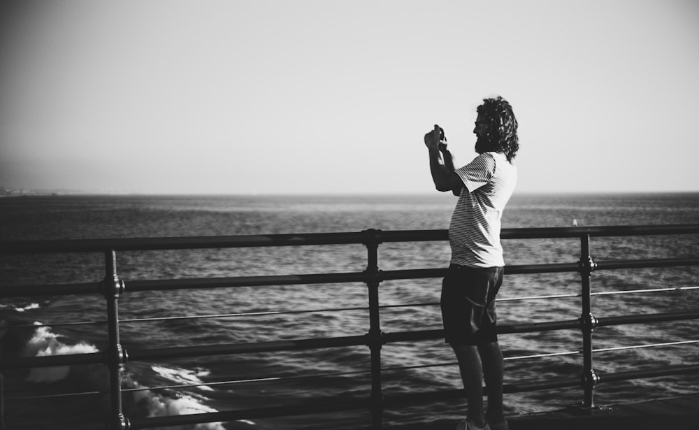 grayscale photo of woman in long sleeve shirt and black pants standing on wooden dock