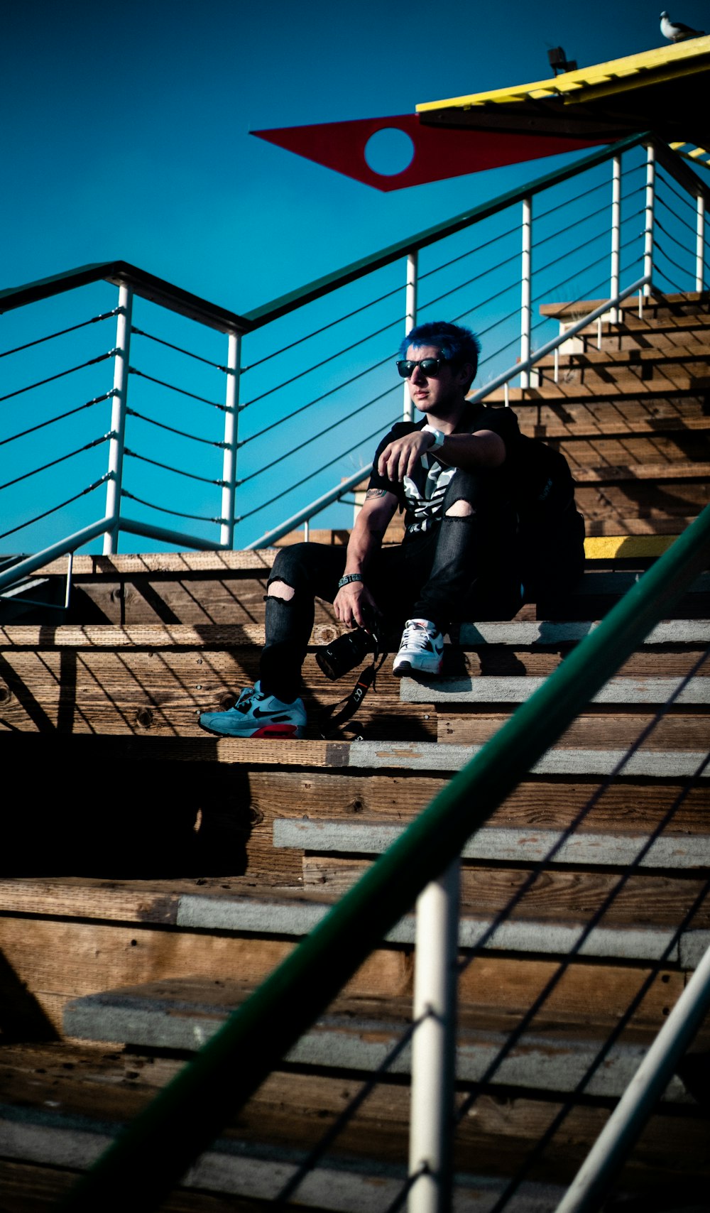 Mann in schwarzem Rundhals-T-Shirt und blauer Jeans sitzt auf einer braunen Holztreppe