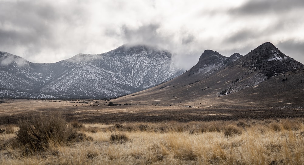 campo de grama marrom perto da montanha sob nuvens brancas durante o dia