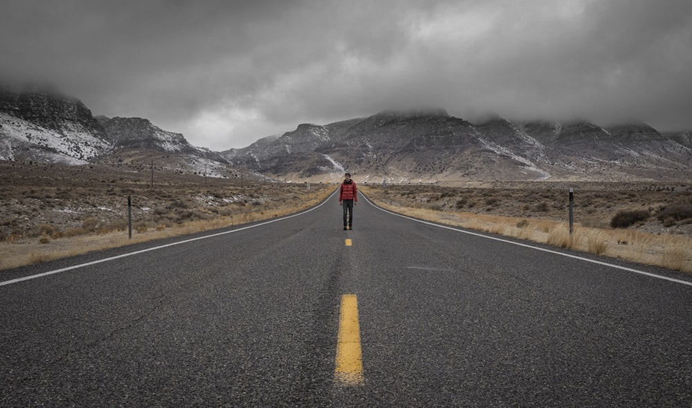 pessoa em jaqueta vermelha andando na estrada de asfalto preto durante o dia