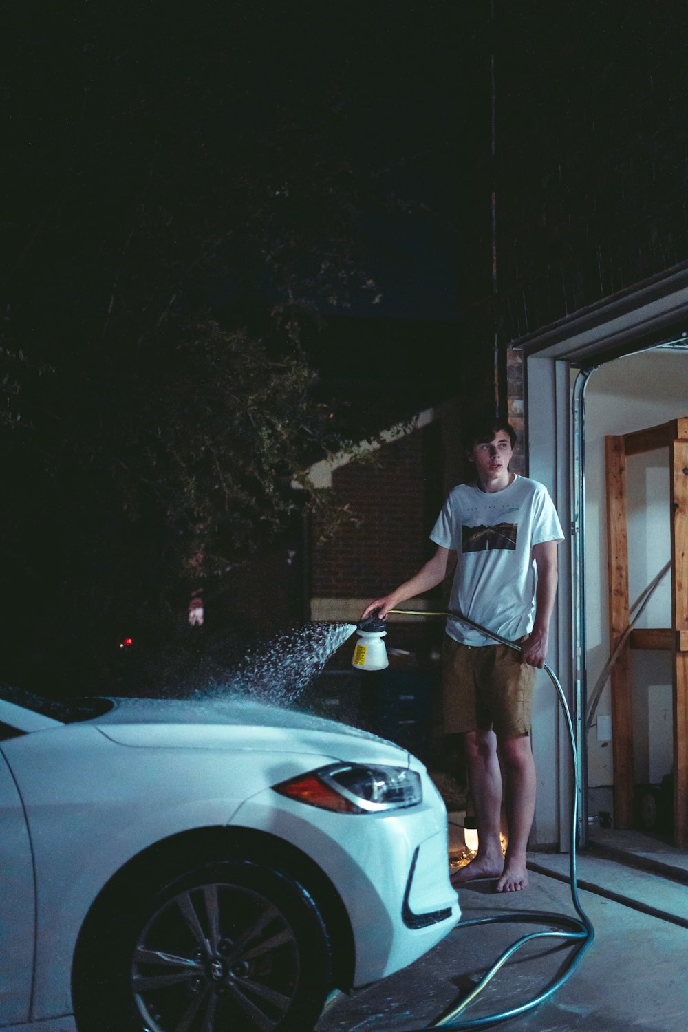 man in white t-shirt and black shorts standing beside white car during night time