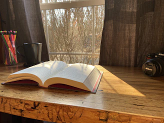 A sunlit café table with an open journal, pastel pens, and a vintage camera.