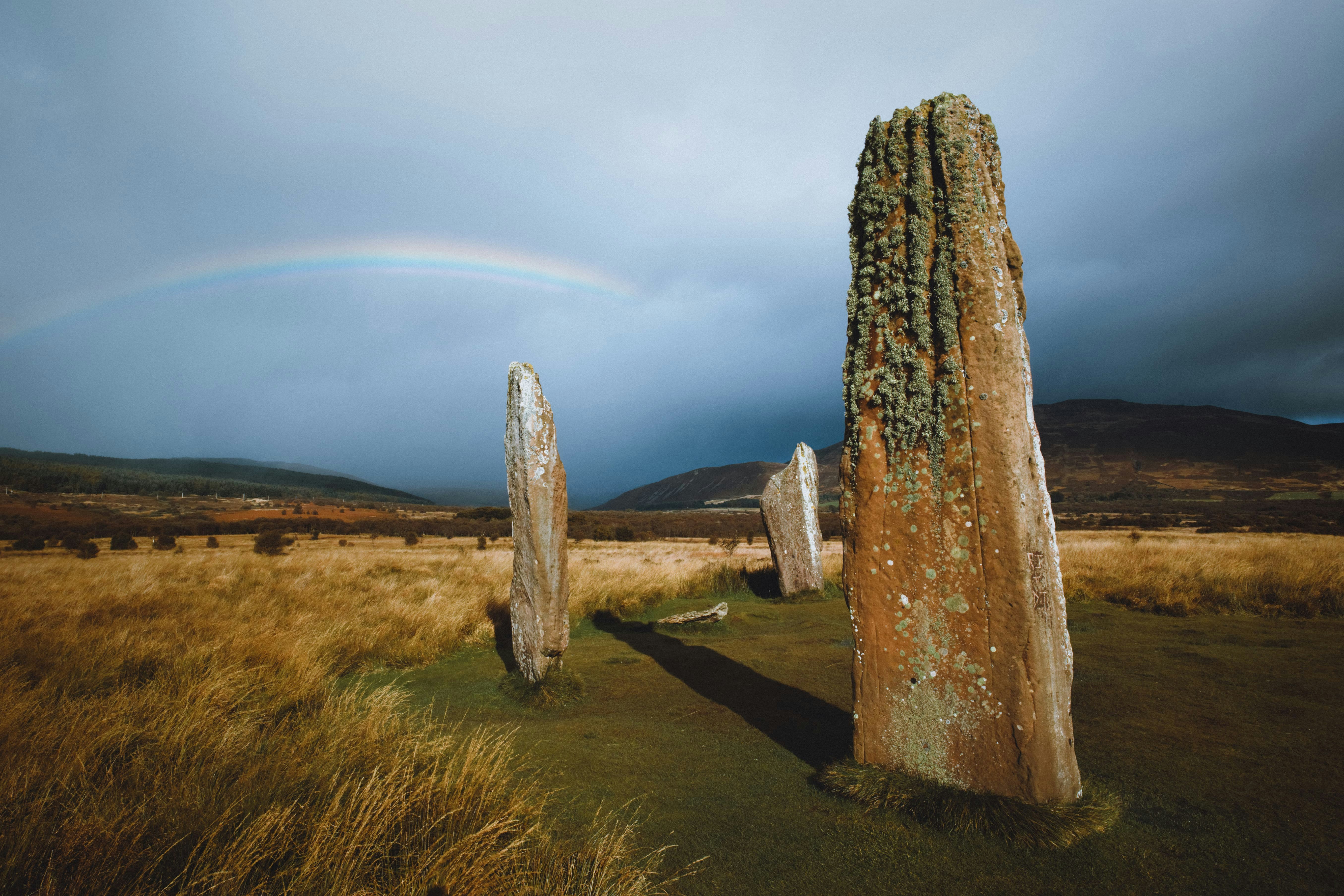 gray rock formation on brown grass field under white clouds during daytime